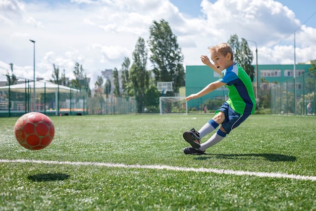 庭のオープンフィールドでサッカーをしている青と緑の形の小さな男の子若いサッカー選手