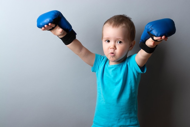 A little boy in boxing gloves and a blue Tshirt on a gray backgroundexpression of emotionscopy space