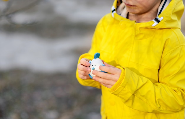 Photo little boy in a bright yellow raincoat playing with easter eggs on the nature, easter concept