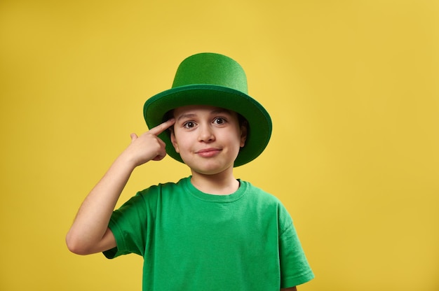 Little boy brings his index finger to his temple standing on a yellow surface