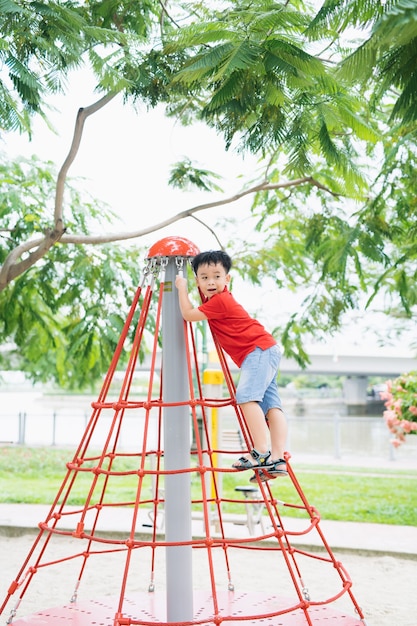 キャップの小さな男の子が公園のジャングルジムに登る