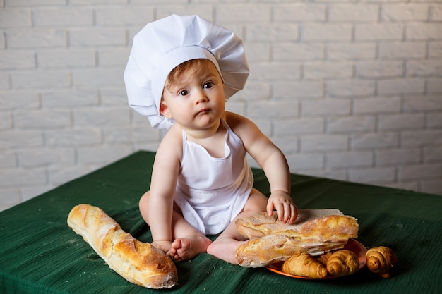 Little boy in a cap and with bread. Little child dressed as a cook in the kitchen.