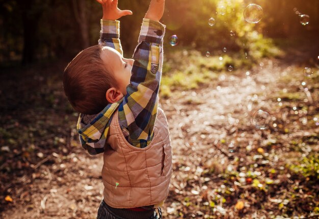 Little boy catching bubbles in autumn forest