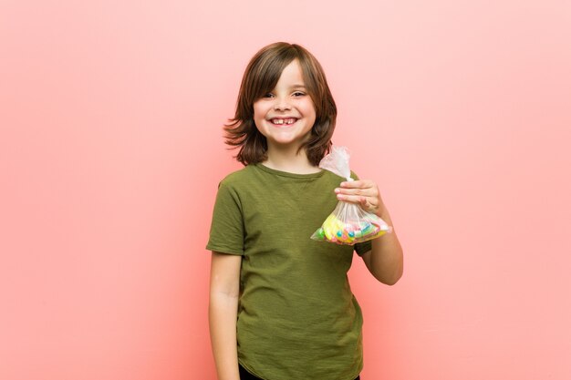 Caramelle caucasiche della tenuta del ragazzino felici, sorridenti e allegre.