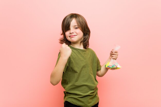 Little boy caucasian holding candies showing fist to camera, aggressive facial expression.