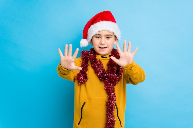 Little boy celebrating christmas day wearing a santa hat isolated showing number ten with hands.