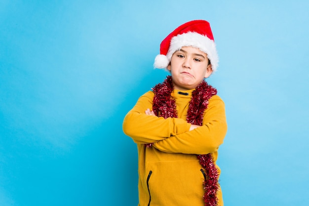 Little boy celebrating christmas day wearing a santa hat isolated unhappy looking in camera with sarcastic expression.