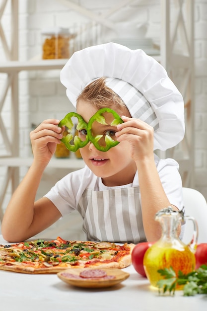 Маленький мальчик в шляпе шеф-повара и фартуке готовит пиццу