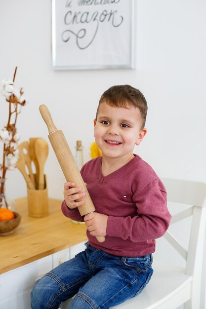 麺棒を手にテーブルの近くで笑顔の小さな男の子シェフめん棒で幸せな子