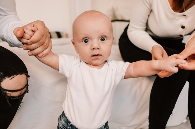 両親と遊んでいる小さな男の子の赤ちゃん、立って歩くことを学び、最初の一歩を踏み出す