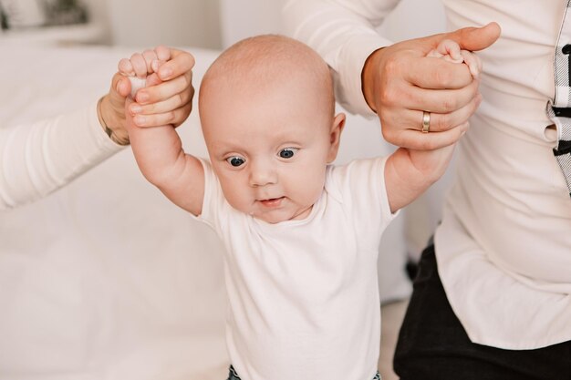 両親と遊ぶ小さな男の子の子供の赤ちゃん、立って歩くことを学び、最初の一歩を踏み出す