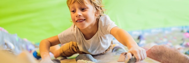 Little boy climbing a rock wall in special boots indoor banner long format