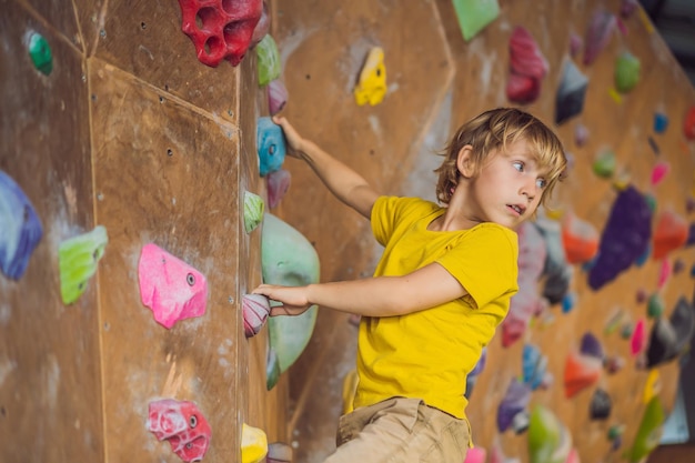 Photo little boy climbing a rock wall in special boots indoor