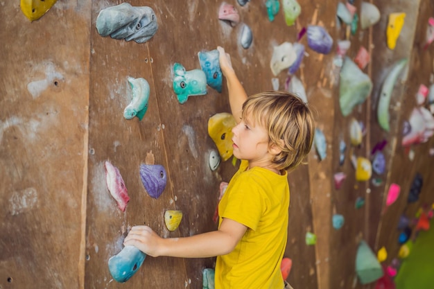 Little boy climbing a rock wall in special boots indoor