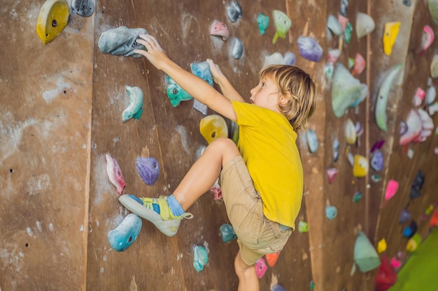 Little boy climbing a rock wall in special boots indoor