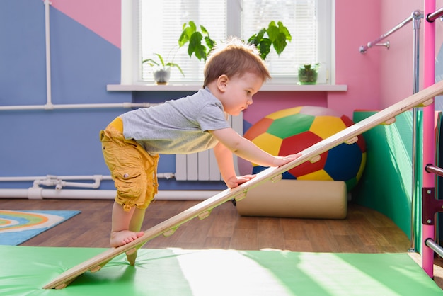 The little boy climbs up a wooden plate in the gym