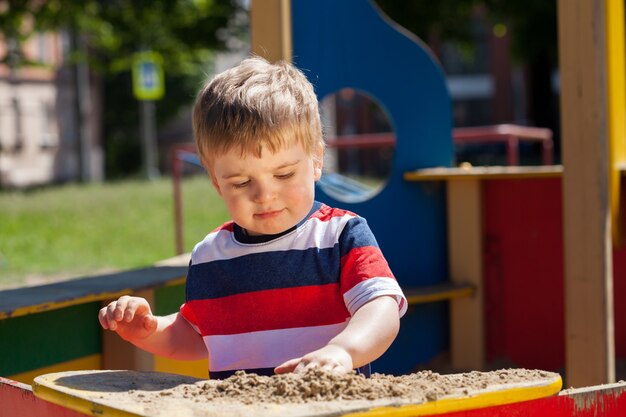 Little boy in a colored T-shirt plays in the sandbox