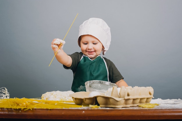 A little boy in cook hat is preparing dinner 