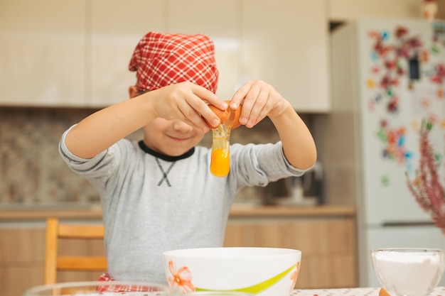 Little boy cooking. Child breaking egg into bowl.