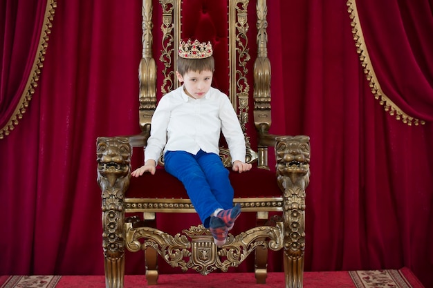 Little boy in a crown in a luxurious chair