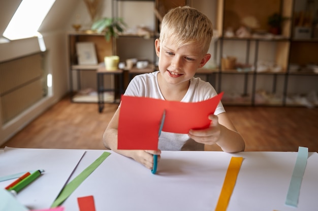 Little boy cuts colored paper, kids in workshop