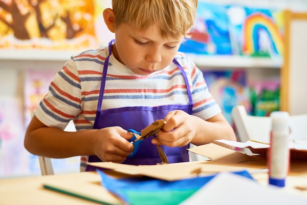 Little boy cutting paper in classe craft