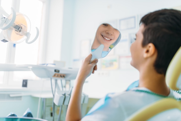 Ragazzino in una poltrona odontoiatrica guardarsi allo specchio i suoi denti, odontoiatria pediatrica, stomatologia dei bambini