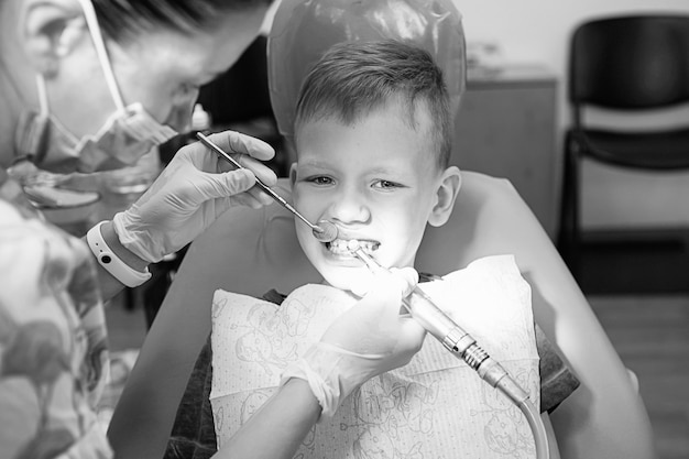 歯科医院の歯科医院の小さな男の子。子供の歯科、小児歯科。黒と白のレトロなスタイルの写真。口腔の健康と衛生