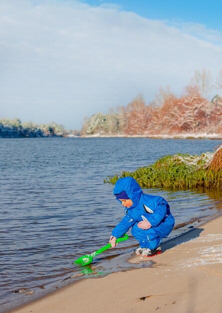 Il ragazzino scava e gioca nella neve invernale, attività invernali per bambini.