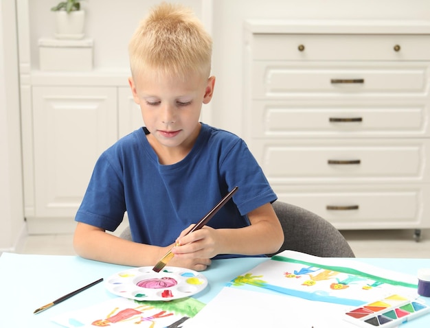 Little boy drawing picture with paint at table indoors