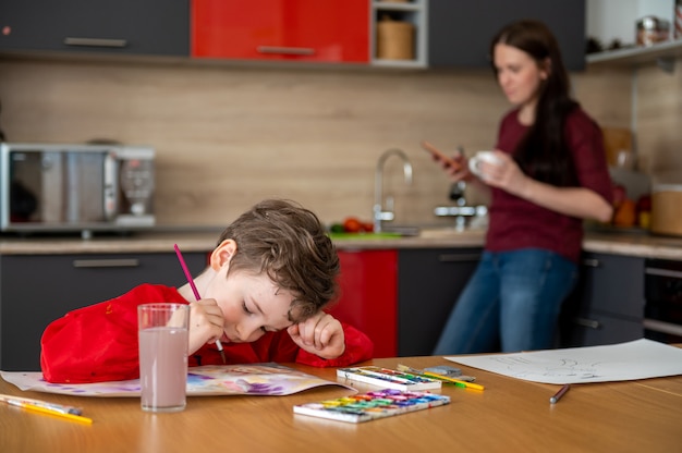 Little boy drawing pictures on kitchen with mom