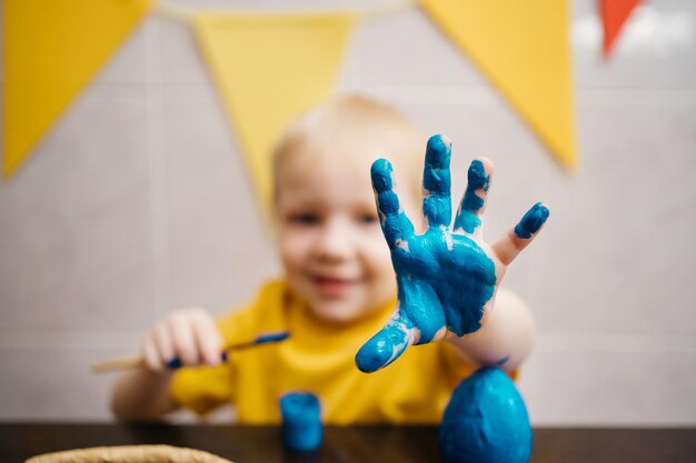 Little boy draws blue paint on his hand paints an easter egg