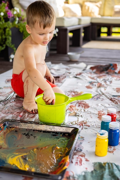 Il ragazzino disegna con mani e piedi con colori a dita su un grande foglio a casa