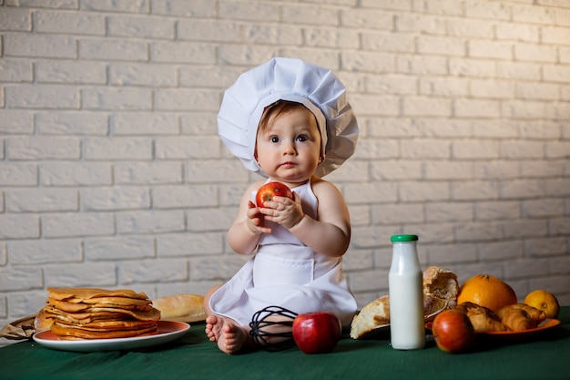 Photo little boy dressed as a cook in the kitchen. handsome child dressed in an apron eating an apple.