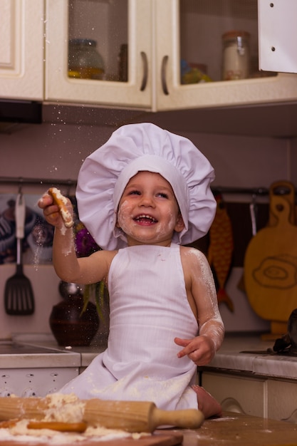 Little boy dressed as a cook kneads flour dough