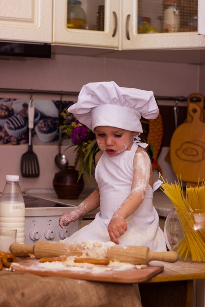 Little boy dressed as a cook kneads flour dough