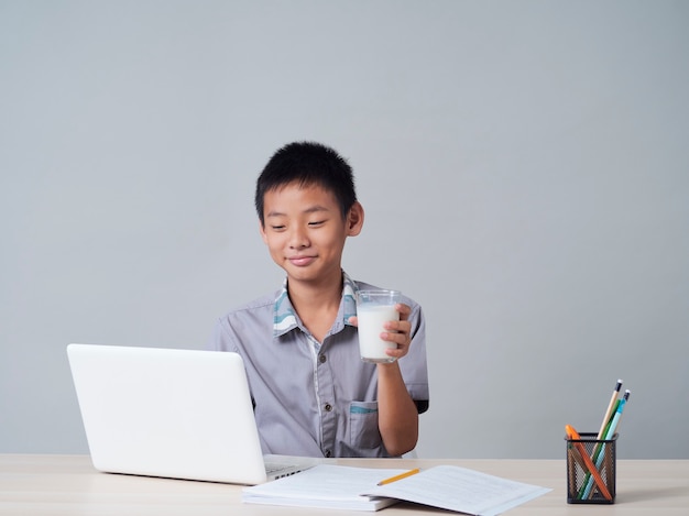 Little boy drinking milk while studying online at home