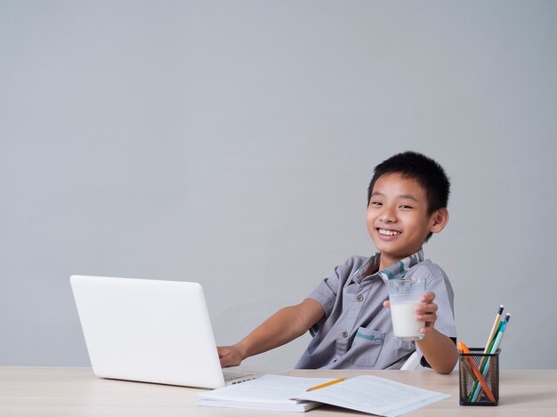 Ragazzino che beve latte mentre studia in linea a casa