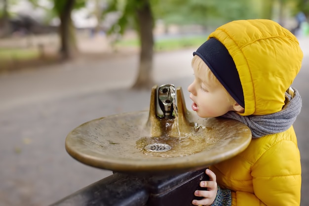 Little boy drinking water from city fountain during walking in Central Park