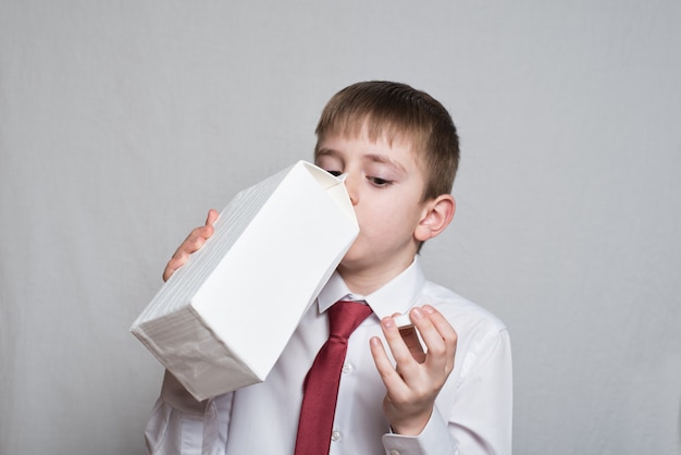 Little boy drinks from a large white package. White shirt and red tie.