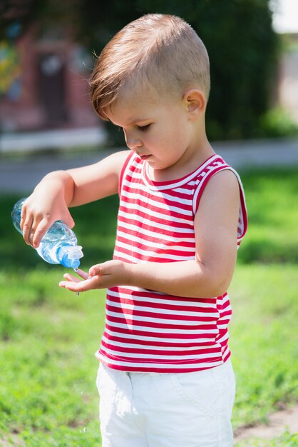 Little boy drinks water from a bottle on a hot day playing on the meadow