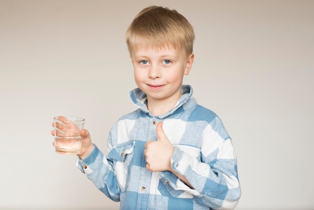 Little boy drinks water from a glass on a gray background in the studio