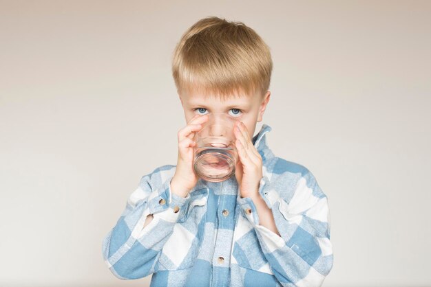 Foto un ragazzino beve acqua da un bicchiere su uno sfondo grigio nello studio