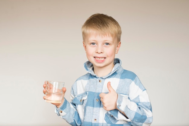 Un ragazzino beve acqua da un bicchiere su uno sfondo grigio nello studio