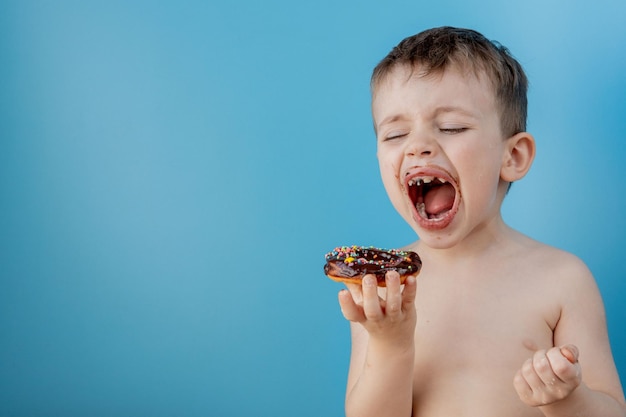 青の背景にドーナツ チョコレートを食べる少年 かわいい幸せな少年彼の口の周りにチョコレートを塗った