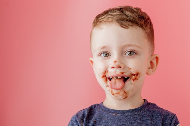 ドーナツチョコレートを食べる少年。口の周りにチョコレートを塗ったかわいい幸せな少年