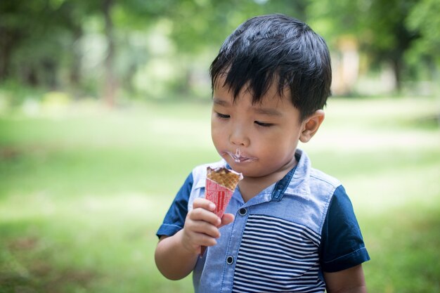 幸せな時間と遊び場でアイスクリームを食べる小さな男の子。