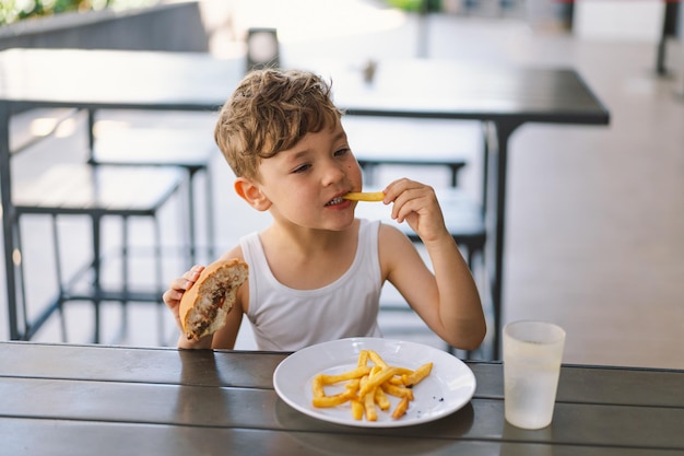 写真 テーブルでサンドイッチとフライドポテトを食べている少年