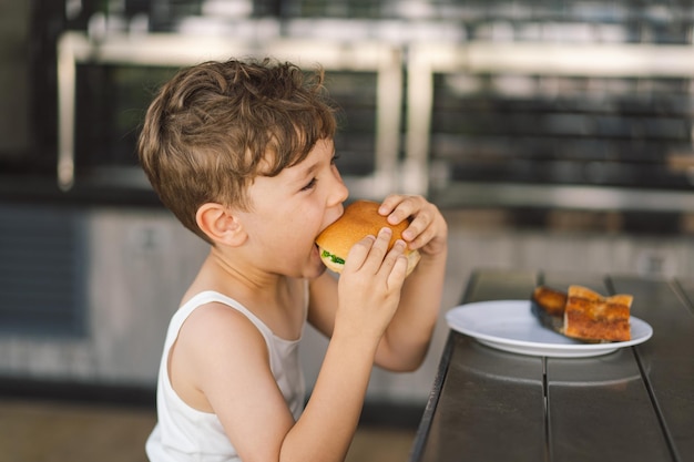 Foto un ragazzino che mangia un panino e delle patatine fritte al tavolo