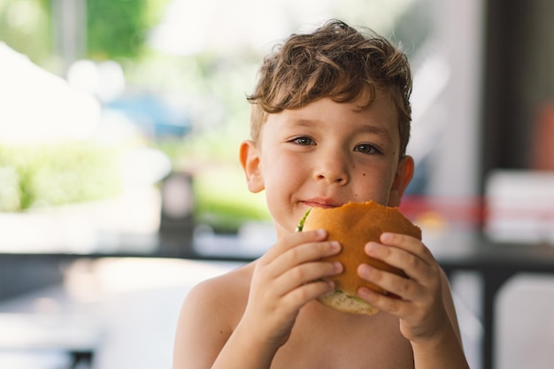 テーブルでサンドイッチとフライドポテトを食べている少年